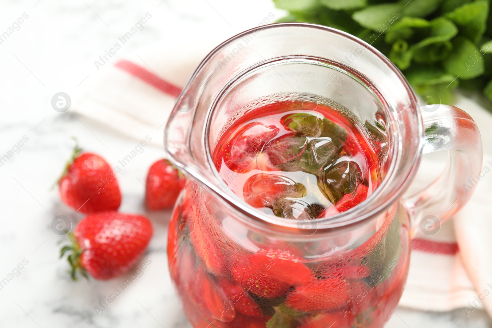 Photo of Tasty strawberry lemonade with mint in jug and berries on white table, closeup