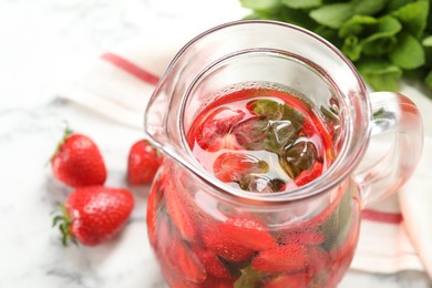 Tasty strawberry lemonade with mint in jug and berries on white table, closeup