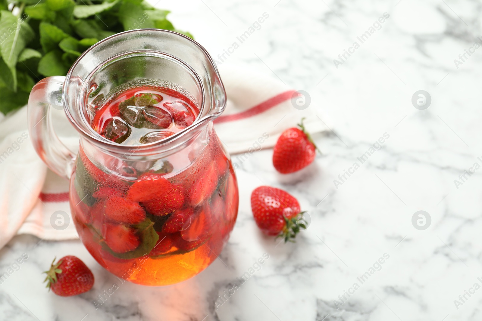 Photo of Tasty strawberry lemonade with mint in jug and berries on white marble table, closeup. Space for text