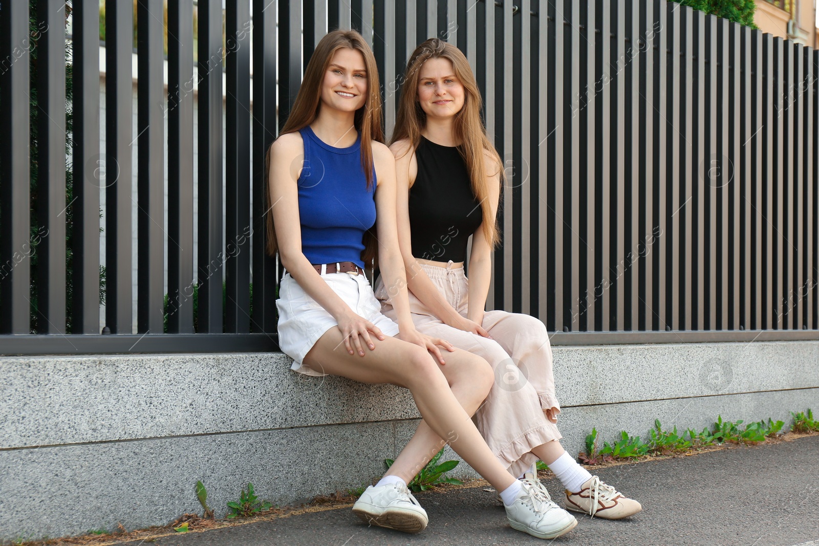 Photo of Two beautiful twin sisters in near metal fence outdoors