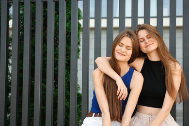 Two beautiful twin sisters in near metal fence outdoors, space for text