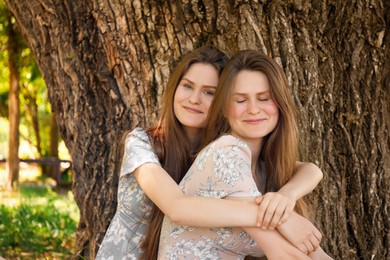 Photo of Two beautiful twin sisters near tree outdoors