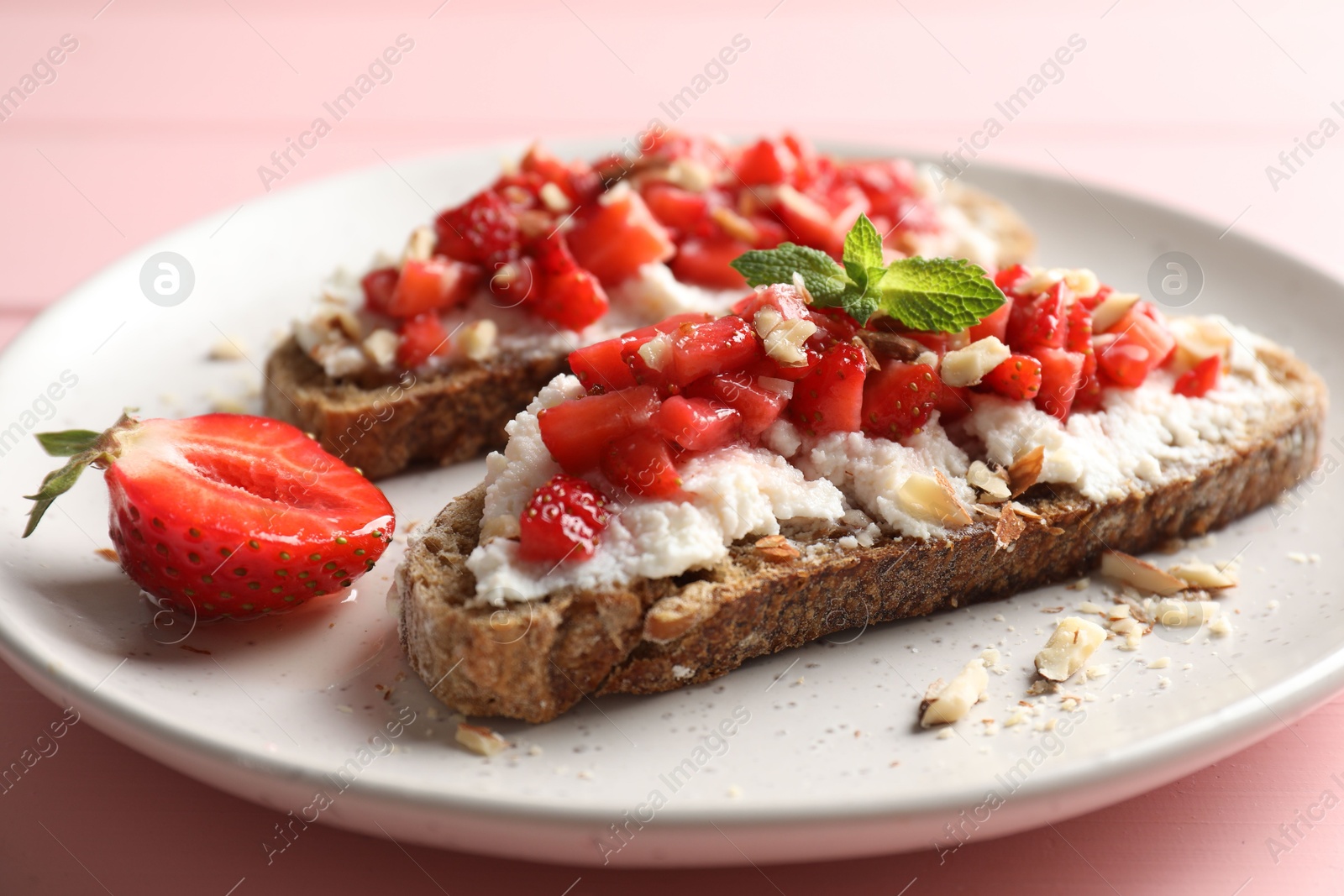 Photo of Bruschettas with ricotta cheese, chopped strawberries and mint on pink wooden table, closeup