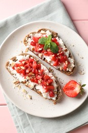 Bruschettas with ricotta cheese, chopped strawberries and mint on pink wooden table, top view