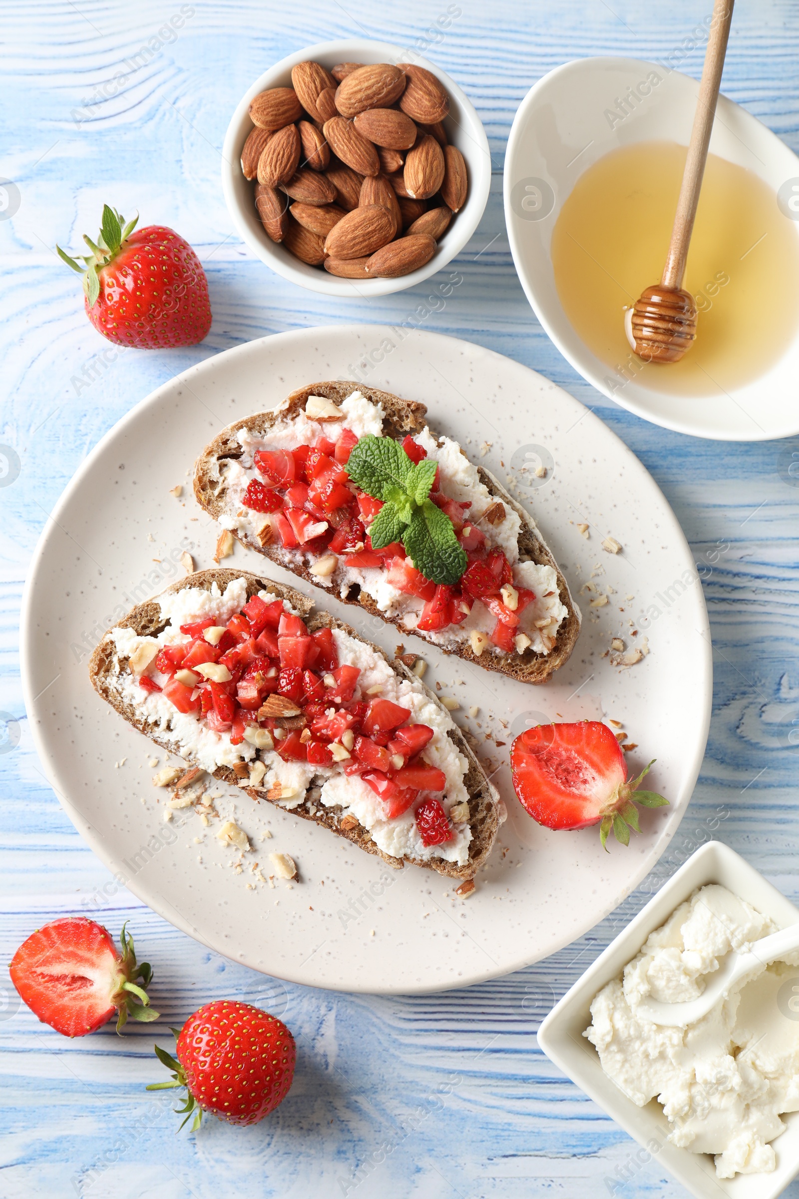 Photo of Bruschettas with ricotta cheese, chopped strawberries and mint on blue wooden table, flat lay