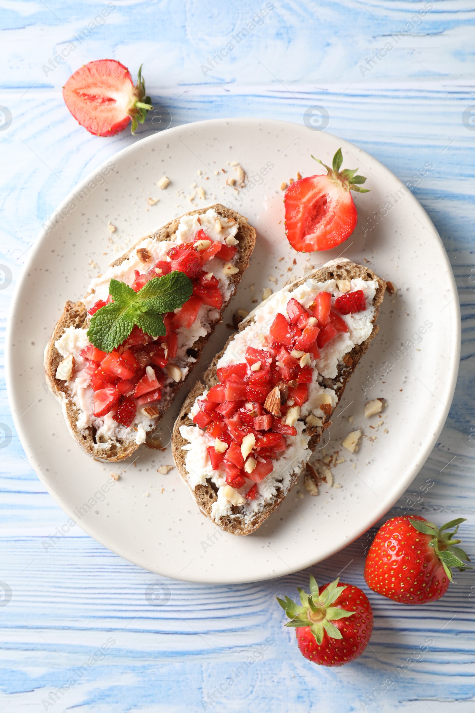 Photo of Bruschettas with ricotta cheese, chopped strawberries and mint on blue wooden table, flat lay