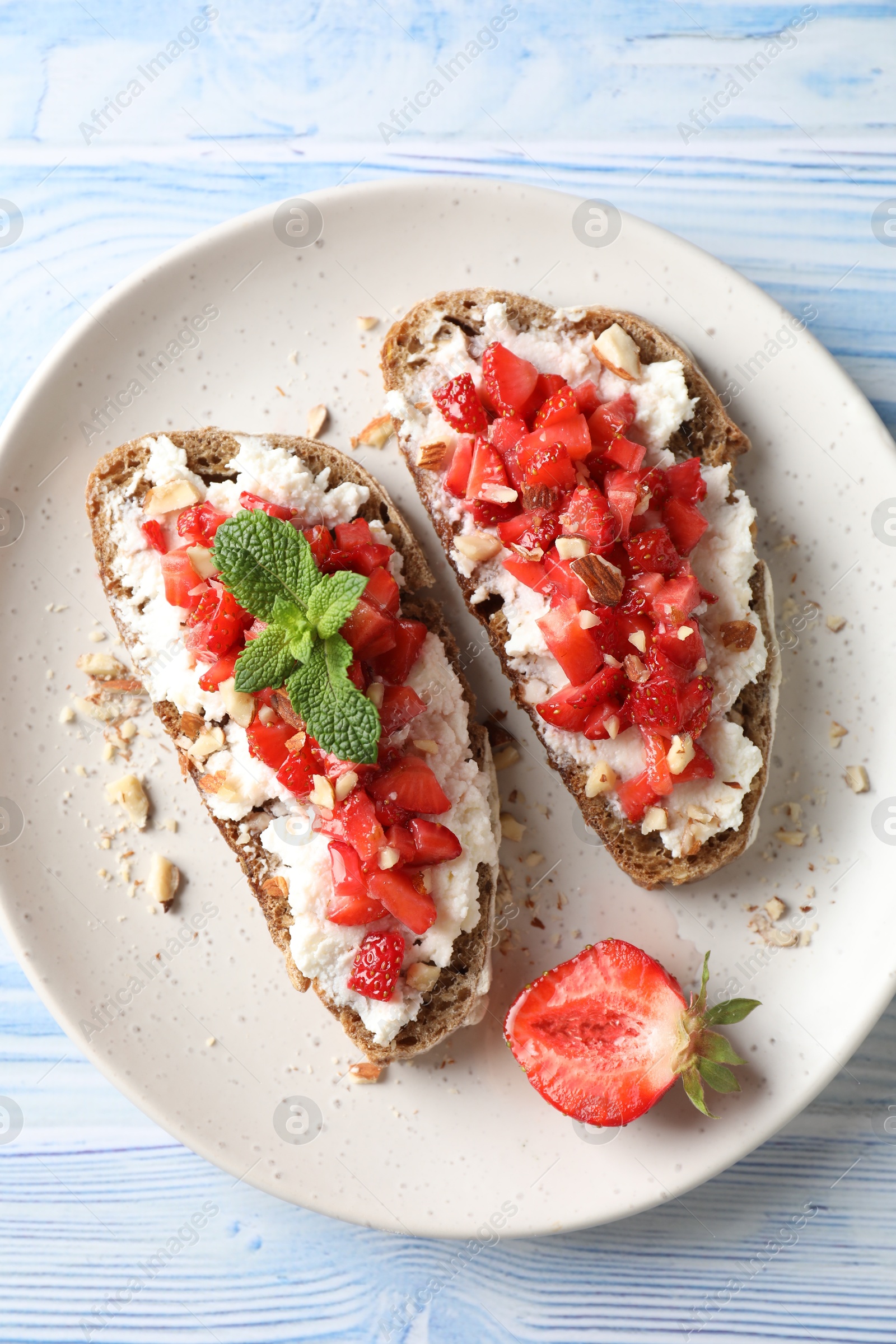 Photo of Bruschettas with ricotta cheese, chopped strawberries and mint on blue wooden table, top view