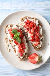 Bruschettas with ricotta cheese, chopped strawberries and mint on blue wooden table, top view