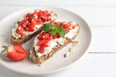 Photo of Bruschettas with ricotta cheese, chopped strawberries and mint on white wooden table, closeup