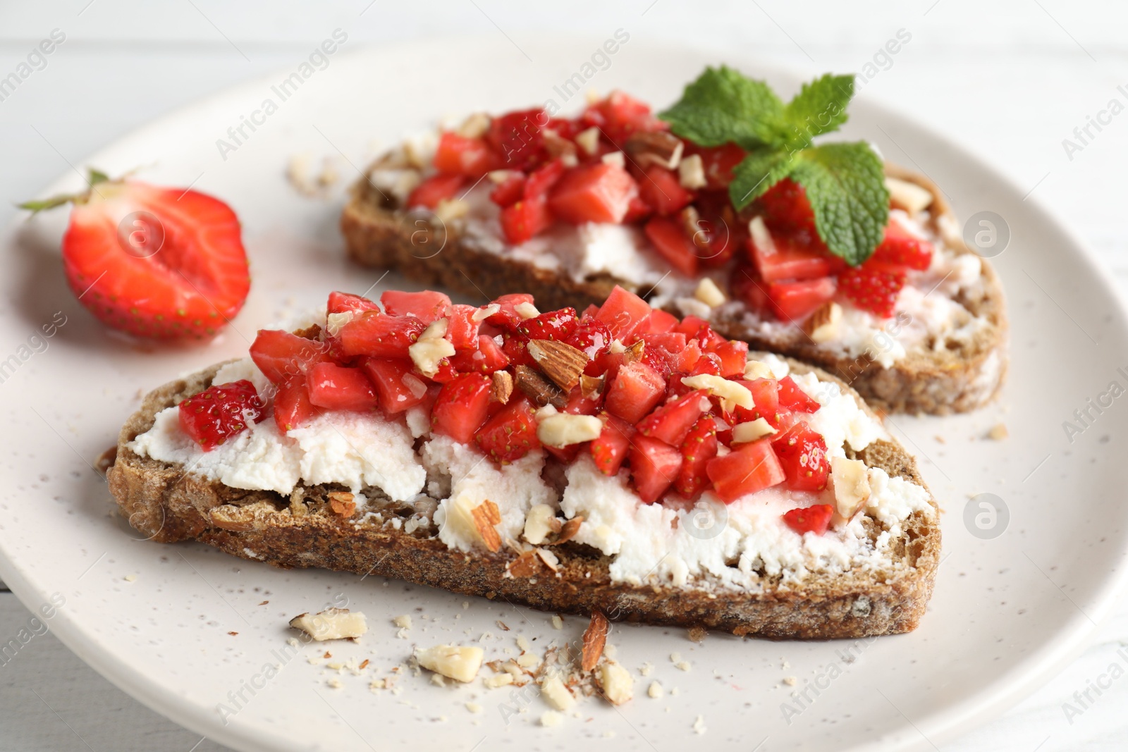 Photo of Bruschettas with ricotta cheese, chopped strawberries and mint on white wooden table, closeup