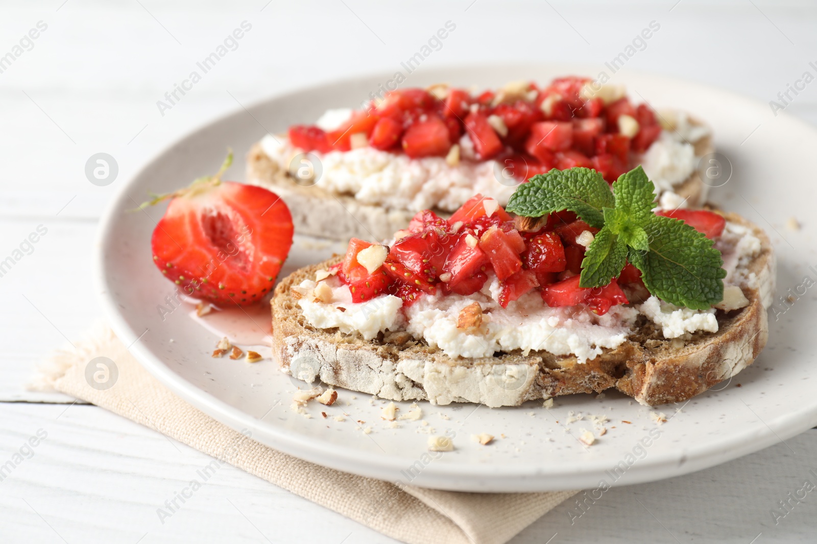 Photo of Bruschettas with ricotta cheese, chopped strawberries and mint on white wooden table, closeup