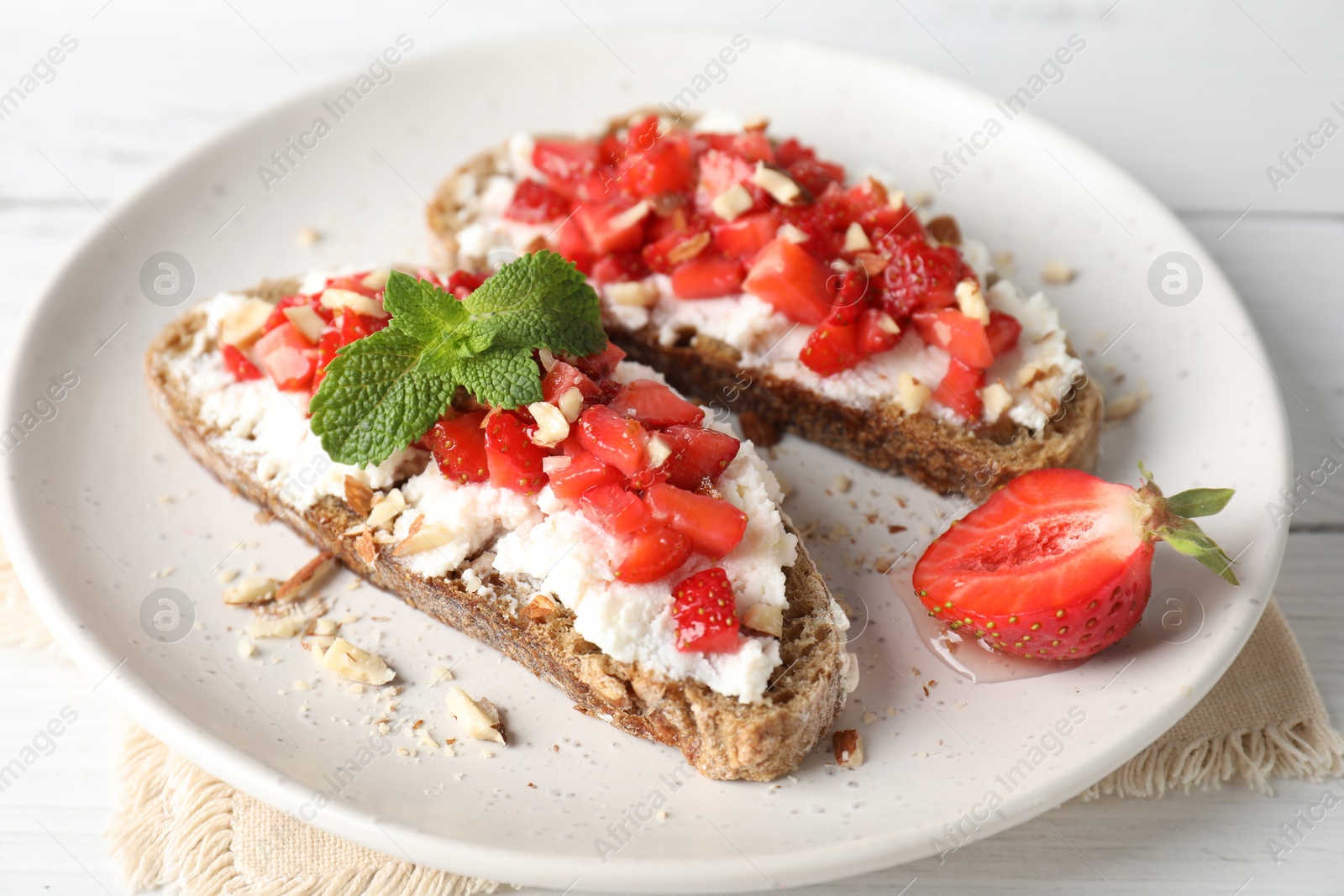 Photo of Bruschettas with ricotta cheese, chopped strawberries and mint on white wooden table, closeup