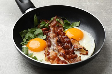 Photo of Tasty bacon, eggs and parsley in frying pan on gray textured table, closeup