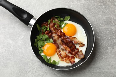 Tasty bacon, eggs and parsley in frying pan on gray textured table, top view