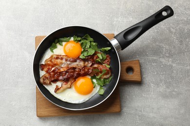 Tasty bacon, eggs and parsley in frying pan on gray textured table, top view