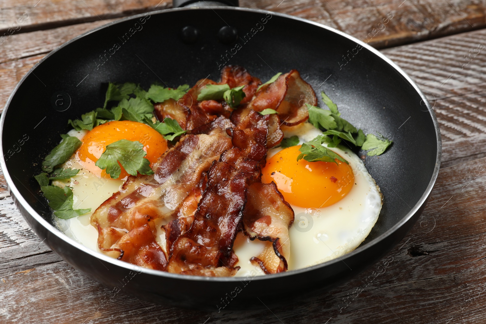 Photo of Tasty bacon, eggs and parsley in frying pan on wooden table, closeup