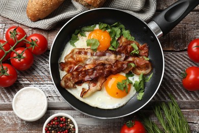 Tasty bacon and eggs in dish among products on wooden table, flat lay