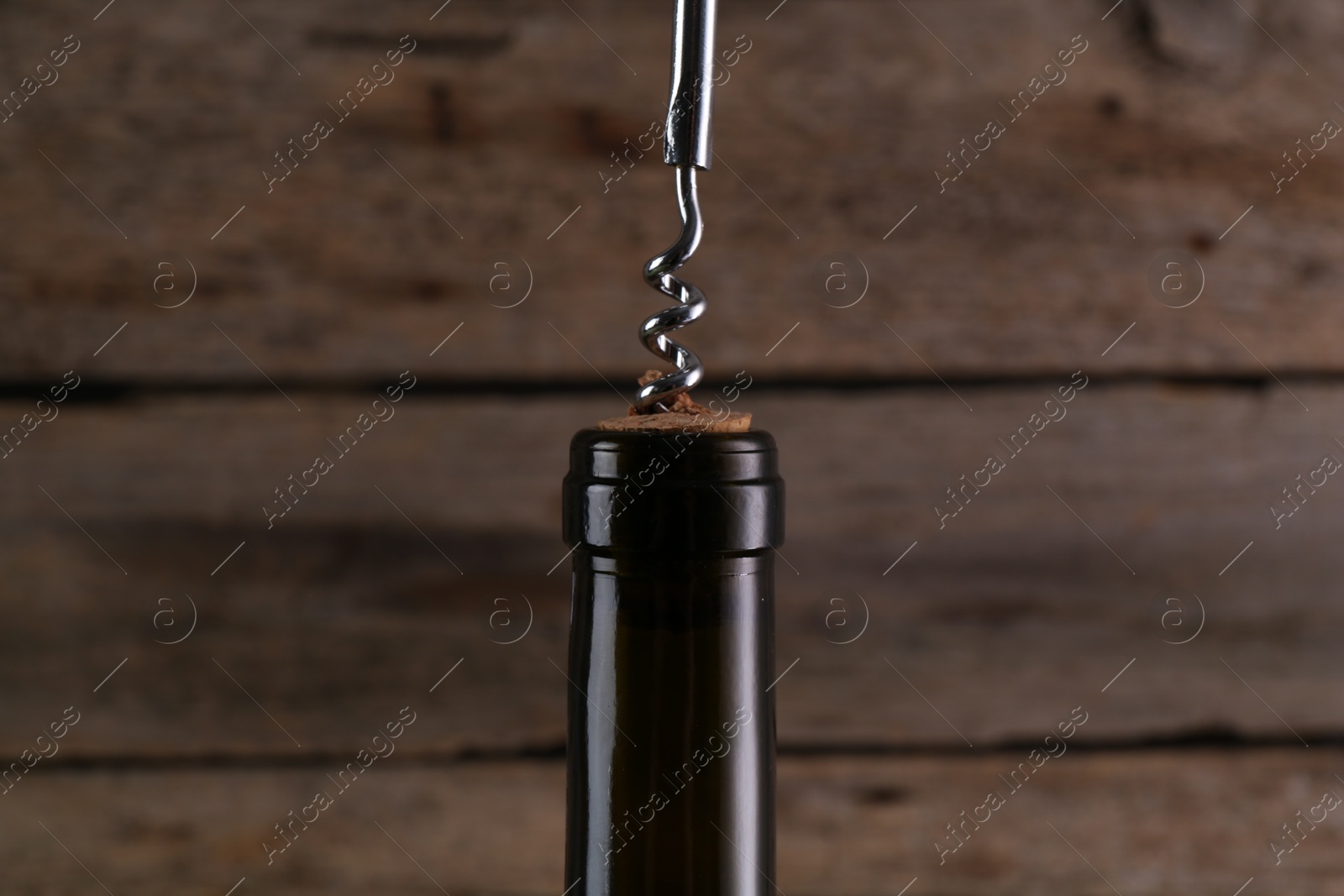 Photo of Wine bottle with corkscrew on wooden background, closeup