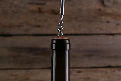 Wine bottle with corkscrew on wooden background, closeup