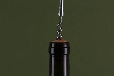 Photo of Wine bottle with corkscrew on olive background, closeup