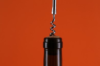 Photo of Wine bottle with corkscrew on orange background, closeup