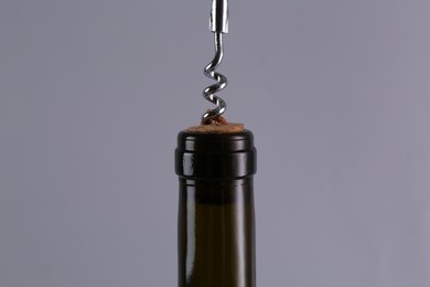 Wine bottle with corkscrew on grey background, closeup