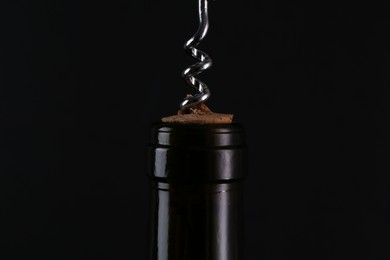 Wine bottle with corkscrew on black background, closeup