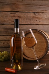 Glass of wine, bottle, corkscrew, barrel and grapes on wooden table