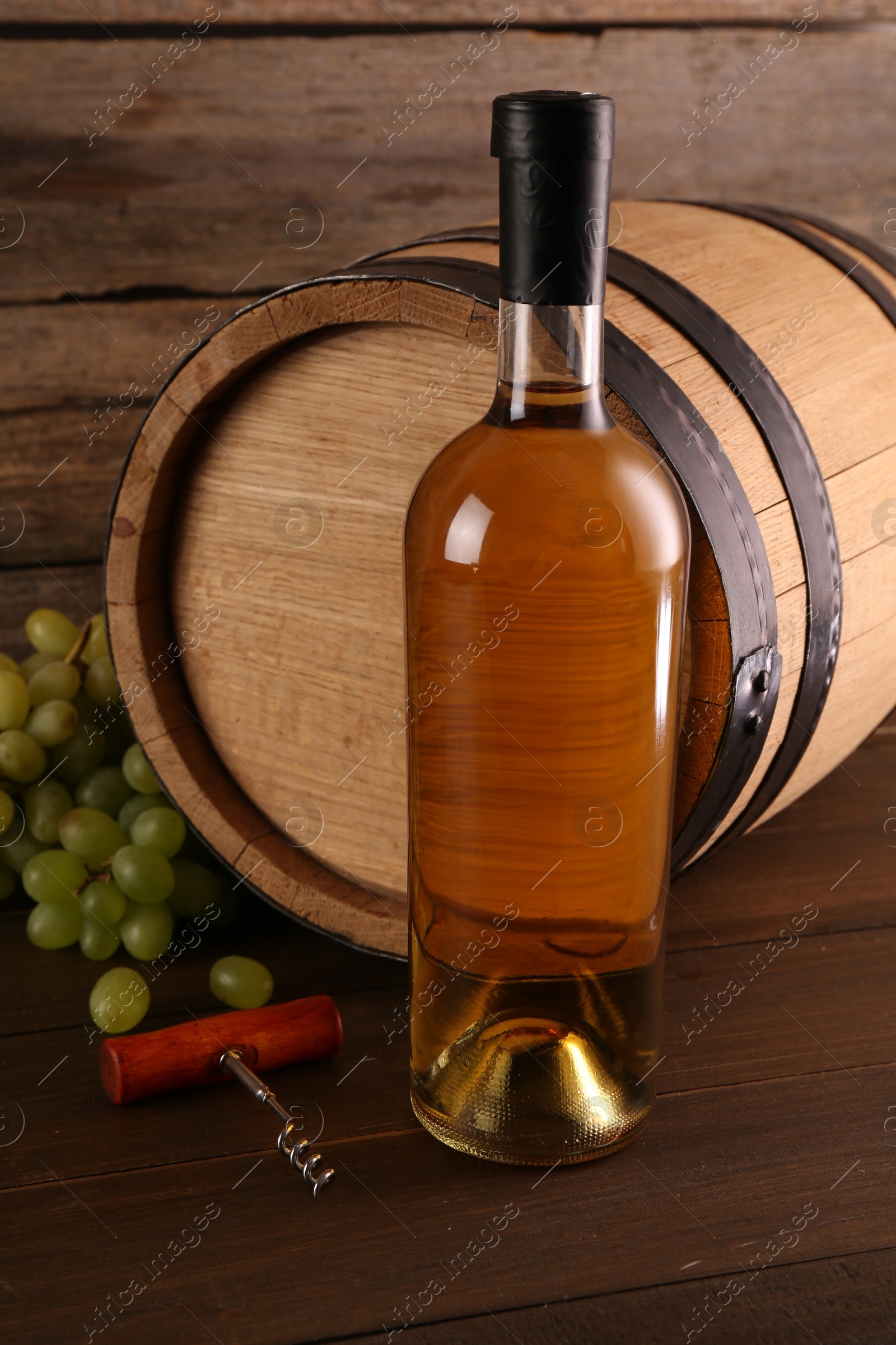 Photo of Bottle of wine, corkscrew, barrel and grapes on wooden table