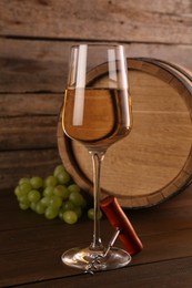 Photo of Glass of wine, corkscrew, barrel and grapes on wooden table