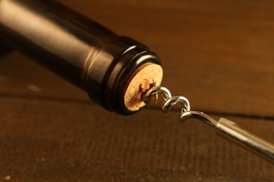 Wine bottle with corkscrew on wooden table, closeup