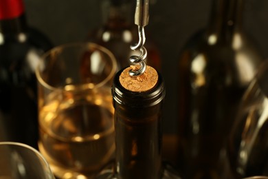 Wine bottle with corkscrew on blurred background, closeup