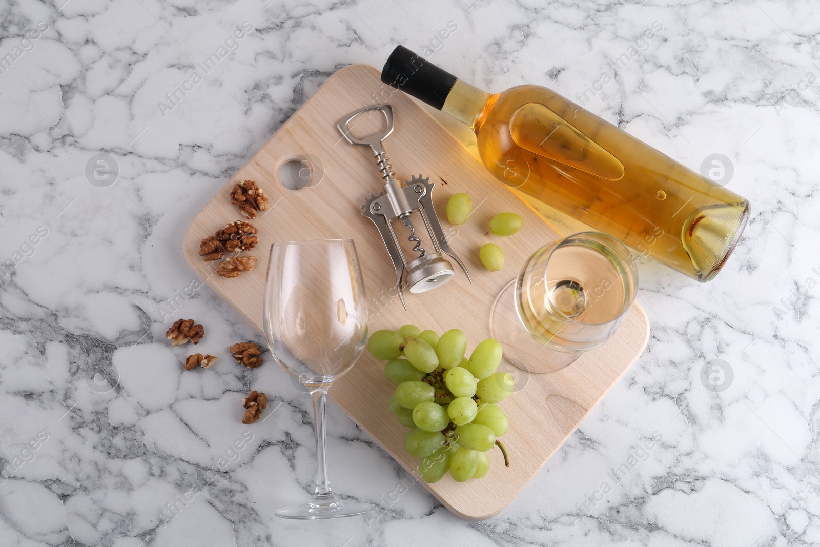 Photo of Wing corkscrew, bottle of wine, glasses, walnuts and grapes on white marble table, top view