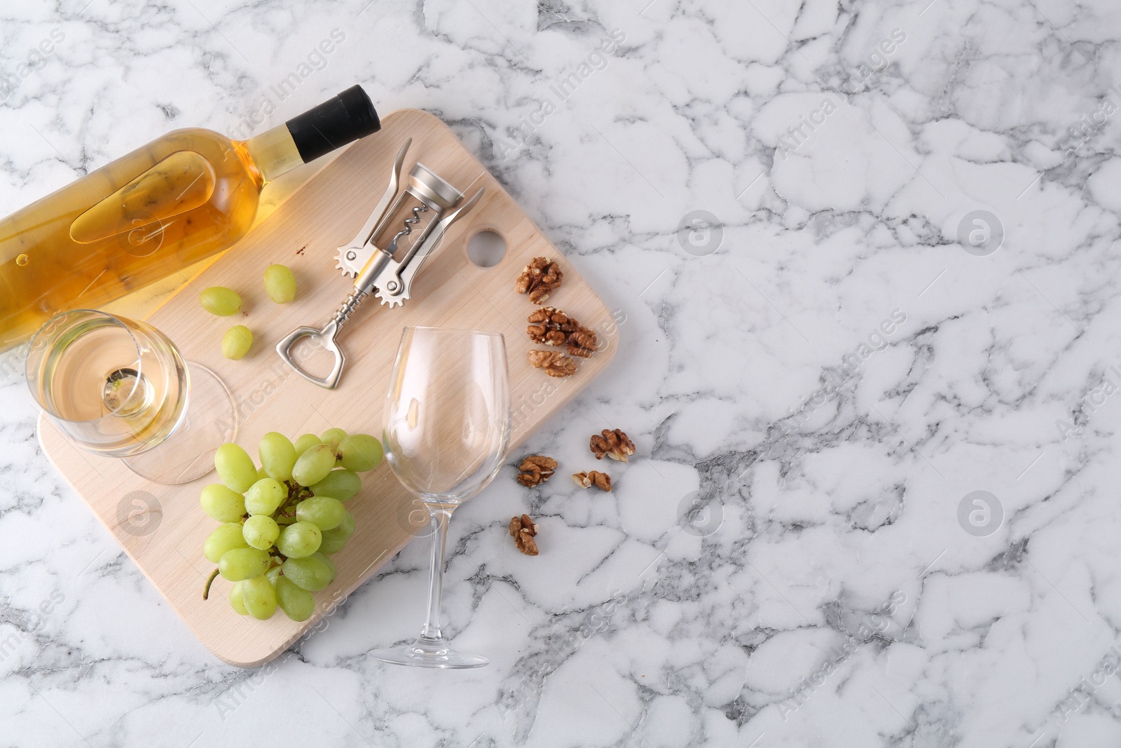 Photo of Wing corkscrew, bottle of wine, glasses, walnuts and grapes on white marble table, top view. Space for text