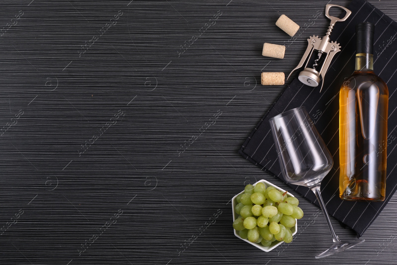 Photo of Wing corkscrew, bottle of wine, glass, corks and grapes on black table, top view. Space for text