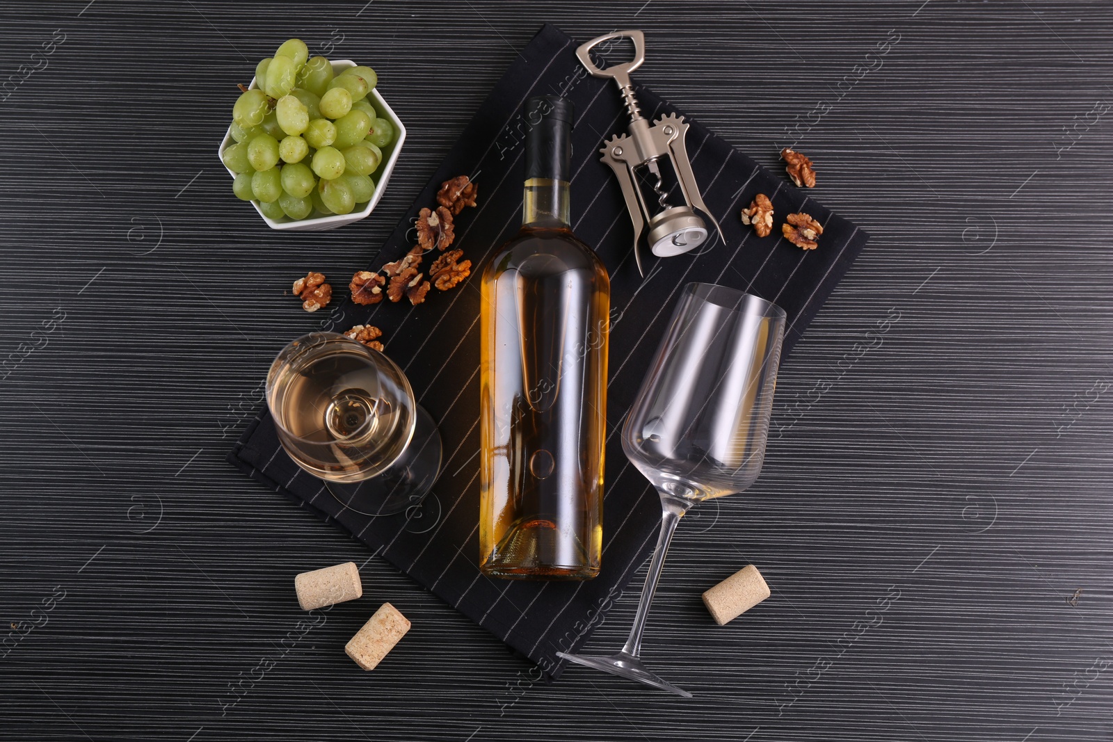 Photo of Wing corkscrew, bottle of wine, glasses, corks, walnuts and grapes on black table, top view