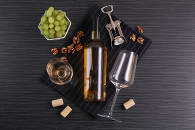 Photo of Wing corkscrew, bottle of wine, glasses, corks, walnuts and grapes on black table, top view