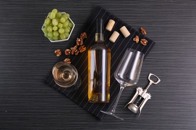 Wing corkscrew, bottle of wine, glasses, corks, walnuts and grapes on black table, top view