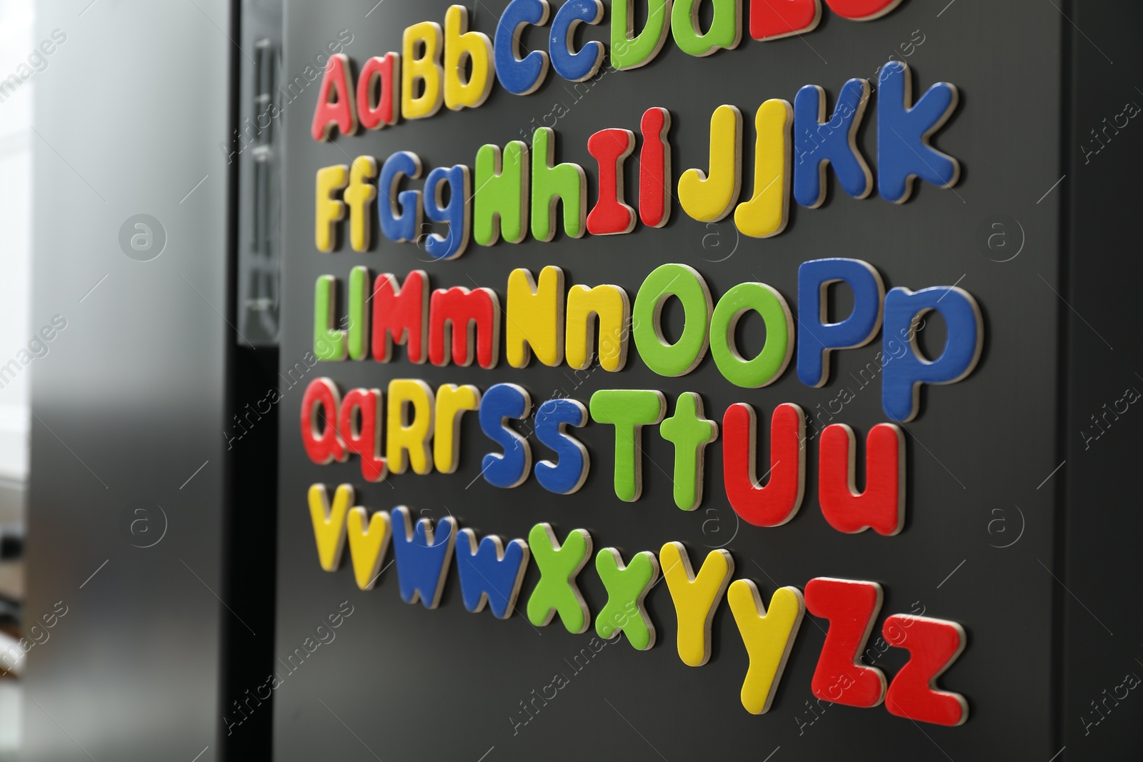 Photo of Alphabetical order. Many bright magnetic letters on fridge indoors