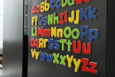 Photo of Alphabetical order. Many bright magnetic letters on fridge indoors