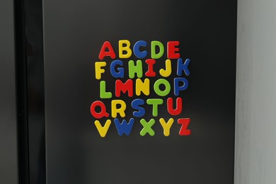 Photo of Alphabetical order. Many bright magnetic letters on fridge indoors