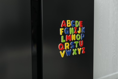 Photo of Alphabetical order. Many bright magnetic letters on fridge indoors