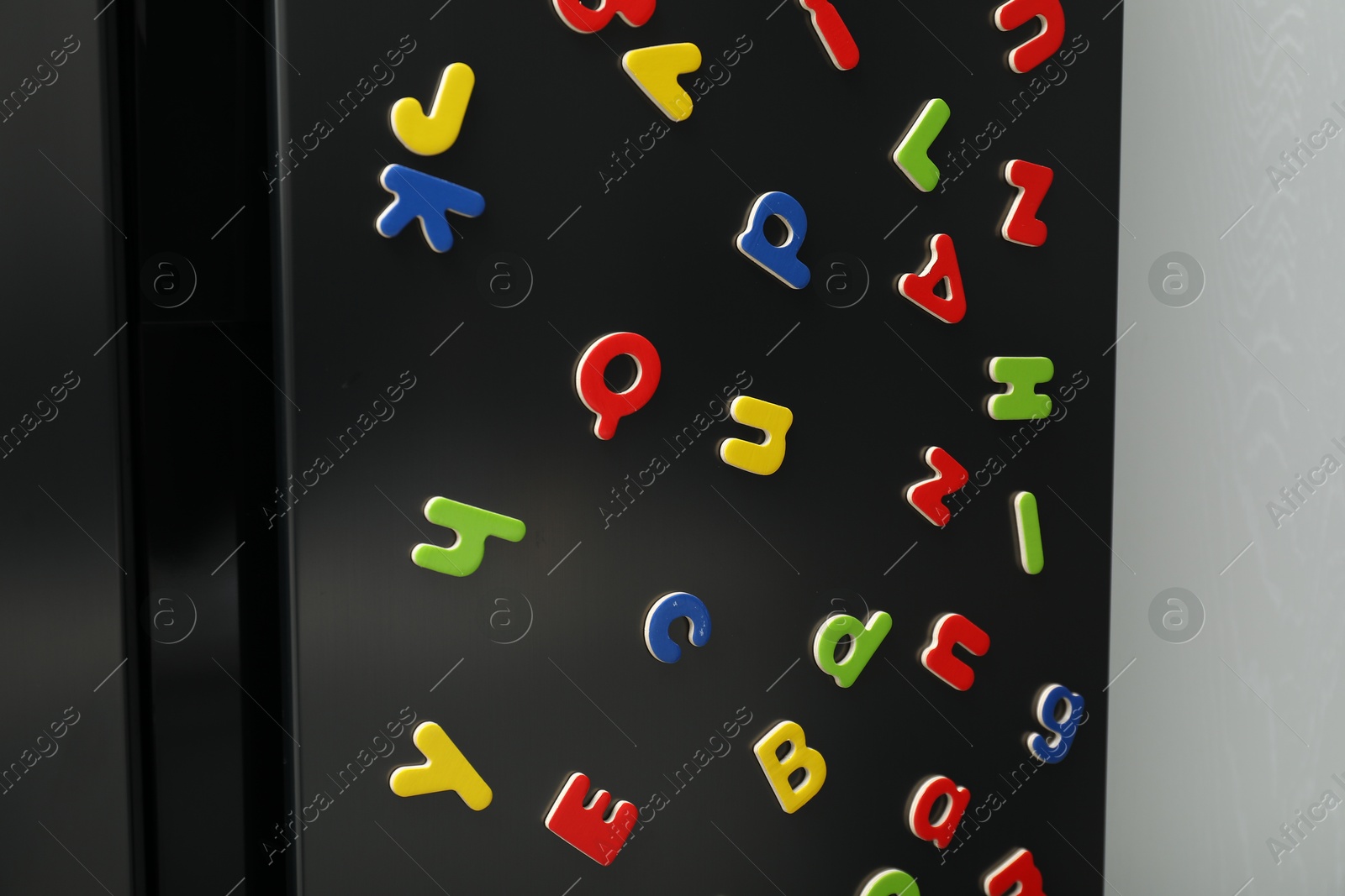 Photo of Many bright magnetic letters on fridge indoors. Learning alphabet