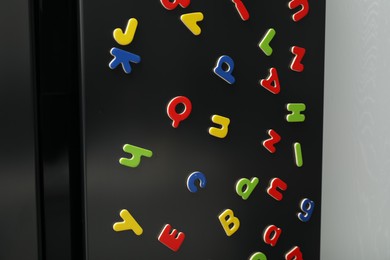 Many bright magnetic letters on fridge indoors. Learning alphabet