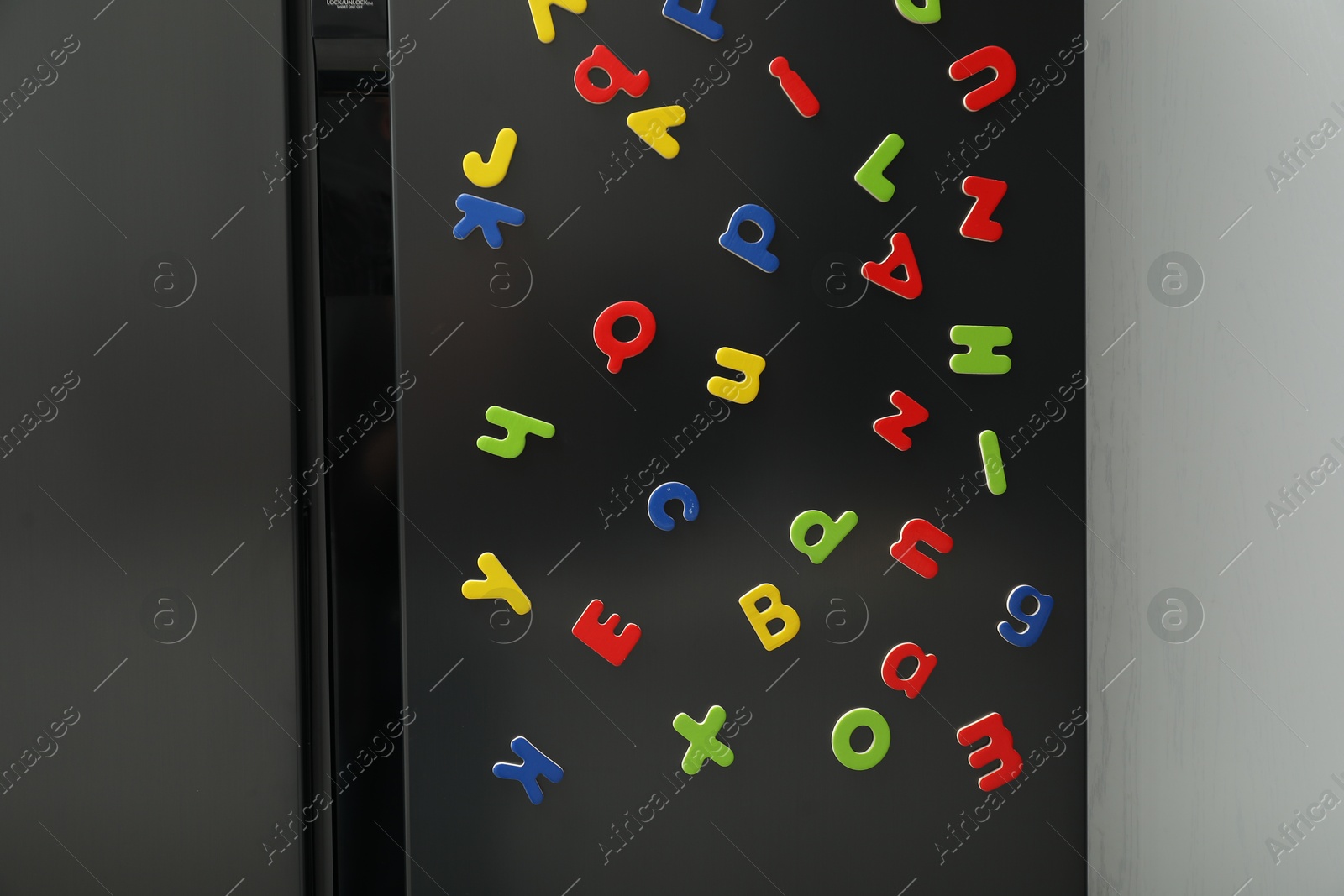 Photo of Many bright magnetic letters on fridge indoors. Learning alphabet