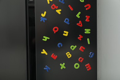 Photo of Many bright magnetic letters on fridge indoors. Learning alphabet