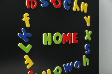 Photo of Word Home and frame made of many bright magnetic letters on fridge indoors. Learning alphabet