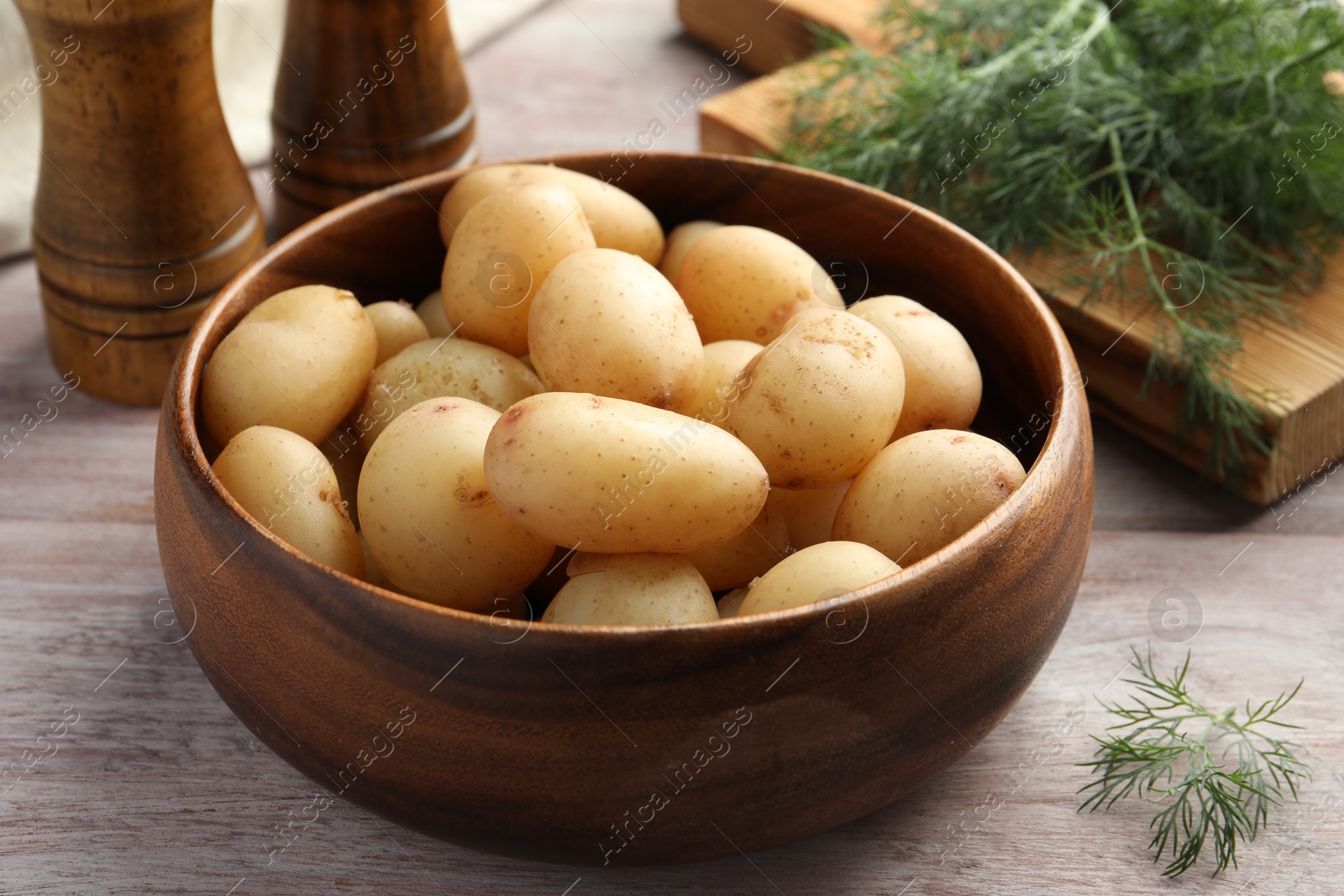 Photo of Boiled potatoes in bowl and dill on wooden table