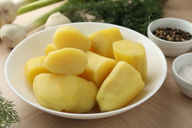 Boiled potatoes in bowl, spices, green onion and dill on wooden table