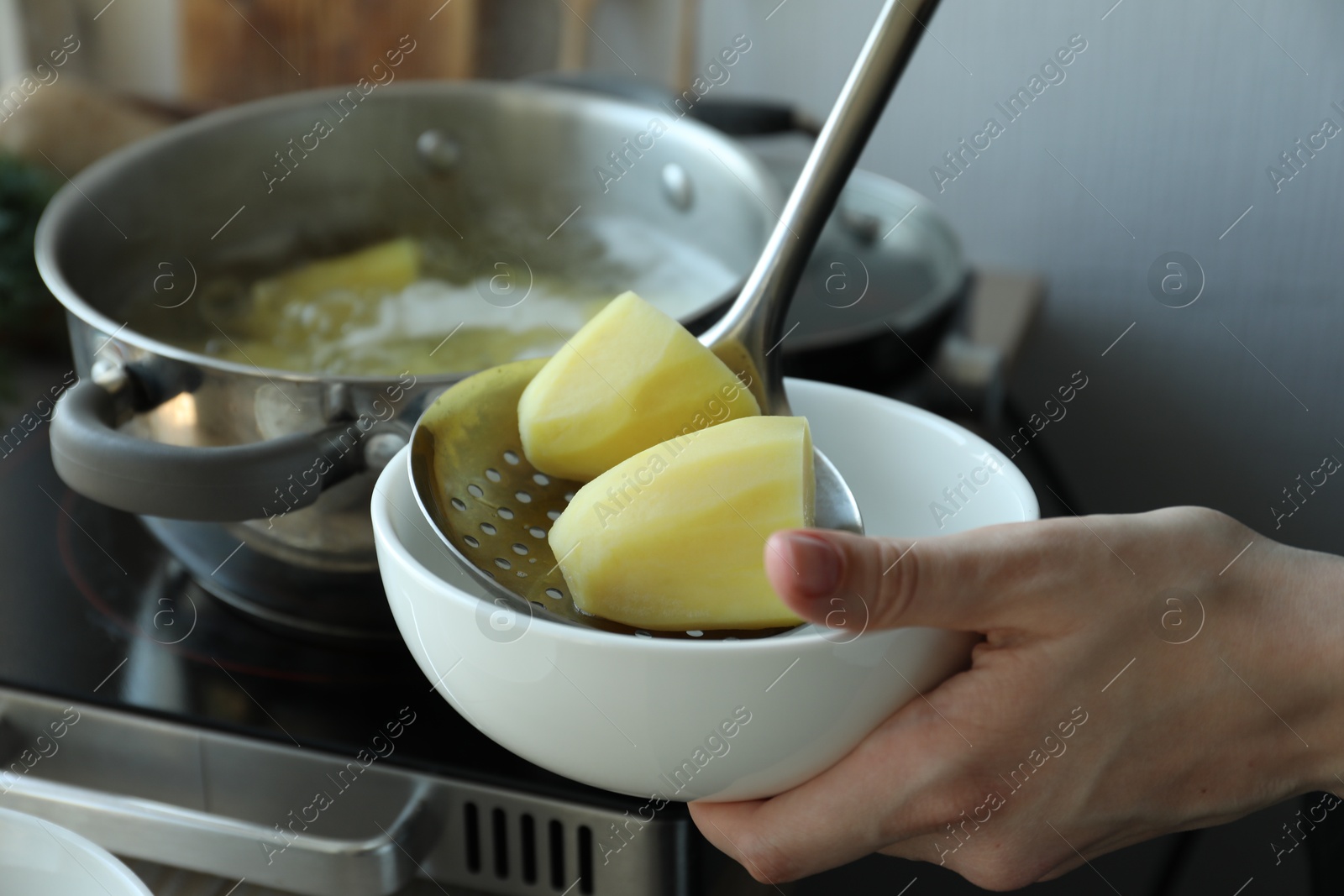 Photo of Woman putting boiled potato into bowl in kitchen, closeup